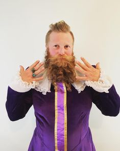 a man with long hair and beard wearing a purple dress holding his hands up to his face