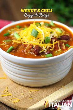 a white bowl filled with chili and cheese on top of a cutting board next to a knife