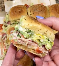 a hand holding a half eaten sandwich with meat and lettuce on it in front of some rolls