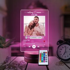 an electronic photo frame sitting on top of a table next to a clock and remote control