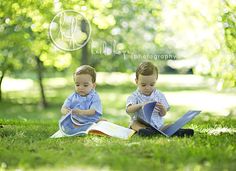 two young boys sitting on the grass reading books together, with trees in the background