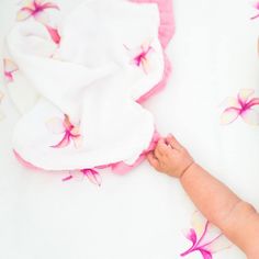 a baby laying on top of a white blanket next to a pink and yellow flower