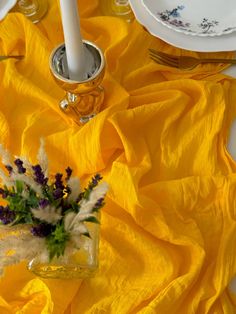 a yellow table cloth with white and purple flowers in a glass vase on the side