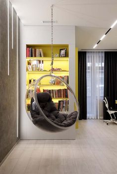 a living room with yellow bookshelves and a hanging chair in the middle of it