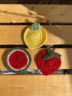 three crocheted fruits sitting on top of a wooden bench next to each other