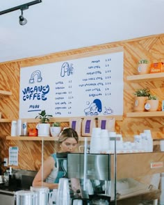 a woman is working behind the counter at a coffee shop in front of a menu