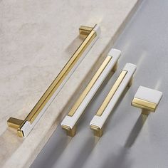 two handles, one with gold and the other white are next to each other on a marble countertop