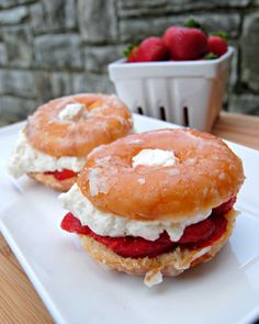 two donuts with cream and strawberries on them sitting on a white square plate