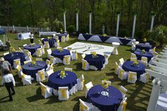 tables and chairs are set up on the lawn for an outdoor wedding reception with blue covers, yellow sashers and white tablecloths