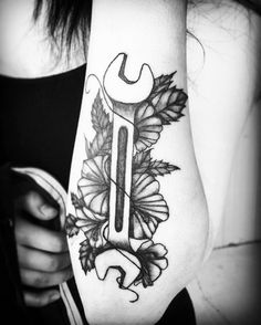 a woman with a tattoo on her arm holding a wrench and some flowers in front of her