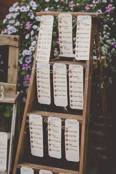 a wooden ladder with seating cards attached to it and purple flowers in the back ground