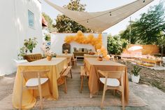 an outdoor dining area with tables and chairs covered in yellow cloths, surrounded by greenery