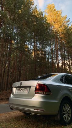 a silver car parked on the side of a road in front of some tall trees