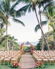 an outdoor ceremony setup with white chairs and floral arrangements on the aisle, surrounded by palm trees