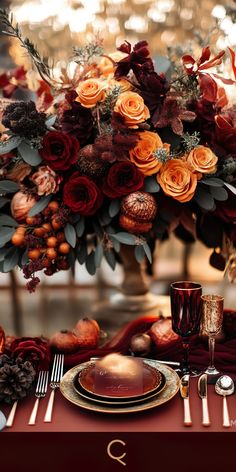 the table is set with red and gold plates, silverware, and orange flowers