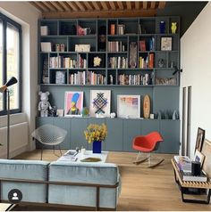 a living room filled with furniture and bookshelves next to a large window on top of a hard wood floor