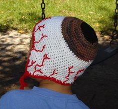 a young boy wearing a crocheted baseball hat on top of a playground swing