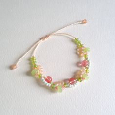 a close up of a beaded bracelet on a white surface with a pink and green cord