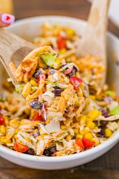 a wooden spoon full of mexican salad with chicken and corn on the side in a white bowl