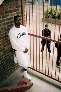 a man standing in front of a gate with his hands on his hips while another man stands behind him