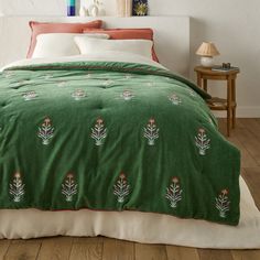 a green bedspread with red and white flowers on it in a bedroom setting