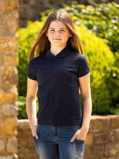 a young woman standing in front of a stone wall wearing a black shirt and jeans