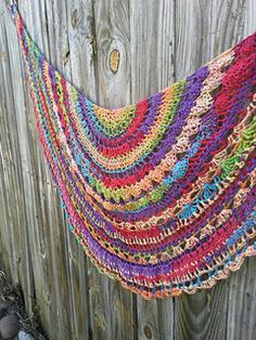 a multicolored crocheted shawl hanging on a wooden fence next to rocks