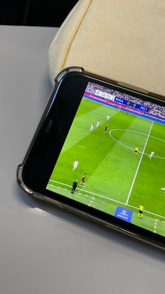 a cell phone sitting on top of a table with a soccer game on the screen