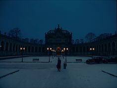 a person standing in front of a building at night with snow on the ground and street lights