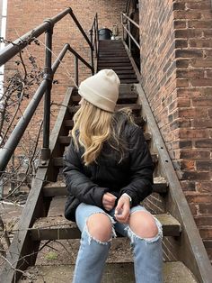 woman sitting on outdoor staircase, head turned the opposite way of the camera, wearing carhartt hat, black puffer jacket, and jeans Brown Beanie Outfit Winter, Cathartic Beanie Outfit, Carhartt Beanie Outfits, Cream Beanie Outfit, Black Beanie Outfit Aesthetic, Cute Beanies Outfits