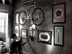 a man sitting on the floor in front of a wall with pictures and a bicycle mounted to it