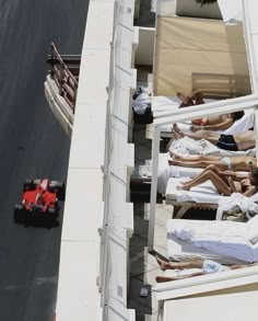 people are laying in beds on the roof of a building and one person is driving a race car