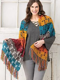 a woman standing in front of a white door wearing a multicolored crocheted shawl