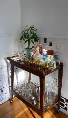 a bar cart filled with liquor bottles and wine glasses sitting on top of a hard wood floor