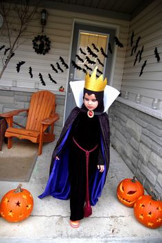 a woman in a costume standing on the front porch with pumpkins and decorations around her