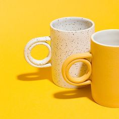 two yellow and white coffee mugs sitting next to each other on a yellow surface