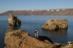 two people standing on rocks near the water