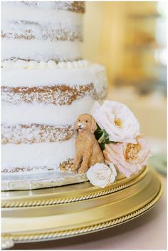 a wedding cake with flowers and a teddy bear on the bottom tier, sitting on a gold plate