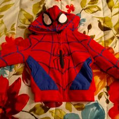 a red spiderman jacket laying on top of a flowery bed spread with flowers