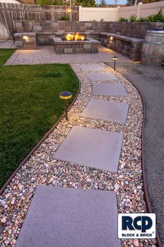 a walkway with lights in the middle of it and grass on both sides, leading to an outdoor fire pit