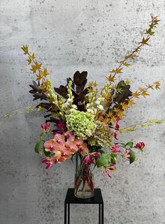 a vase filled with lots of flowers on top of a black table next to a wall