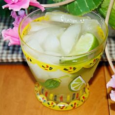 a glass filled with ice and lemon slices on top of a wooden table next to flowers