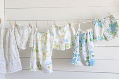 baby clothes hanging on a line in front of a white wall with wood planks