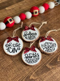 four wooden ornaments with red and white ribbon on them sitting next to a string of beads