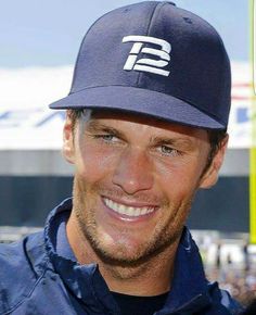 a close up of a person wearing a baseball cap and smiling at the camera with other people in the background