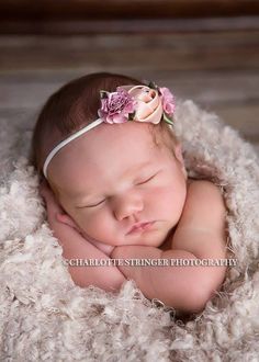 a newborn baby is sleeping in a pile of fluffy white blankets and wearing a pink flower headband