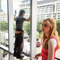 a woman standing in front of a window next to a young man on a balcony