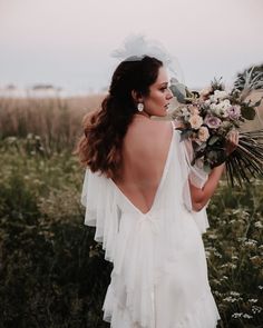 a woman in a white dress holding a bouquet and looking off into the distance with her back to the camera