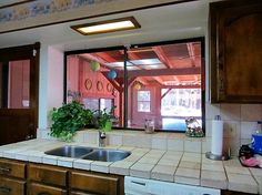 a kitchen with wooden cabinets and white tile counter tops is seen through the open window