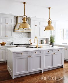 an instagramted photo of a kitchen with white cabinets and gold pendant lights over the island